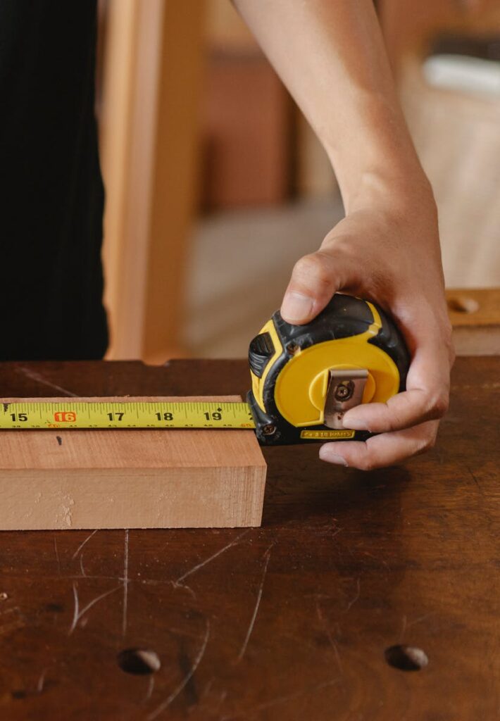 Close-up of carpenter's hand measuring wood with a tape measure in a workshop.